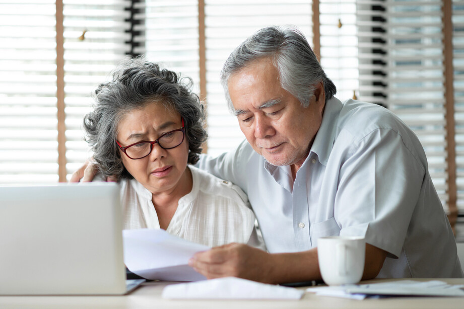 older Asian couple looking at papers and a computer