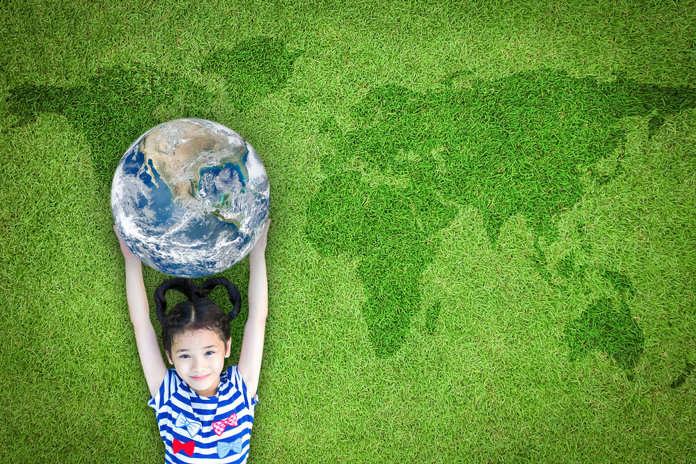 girl holding globe above head while laying on grass that has darker grass showing map of world