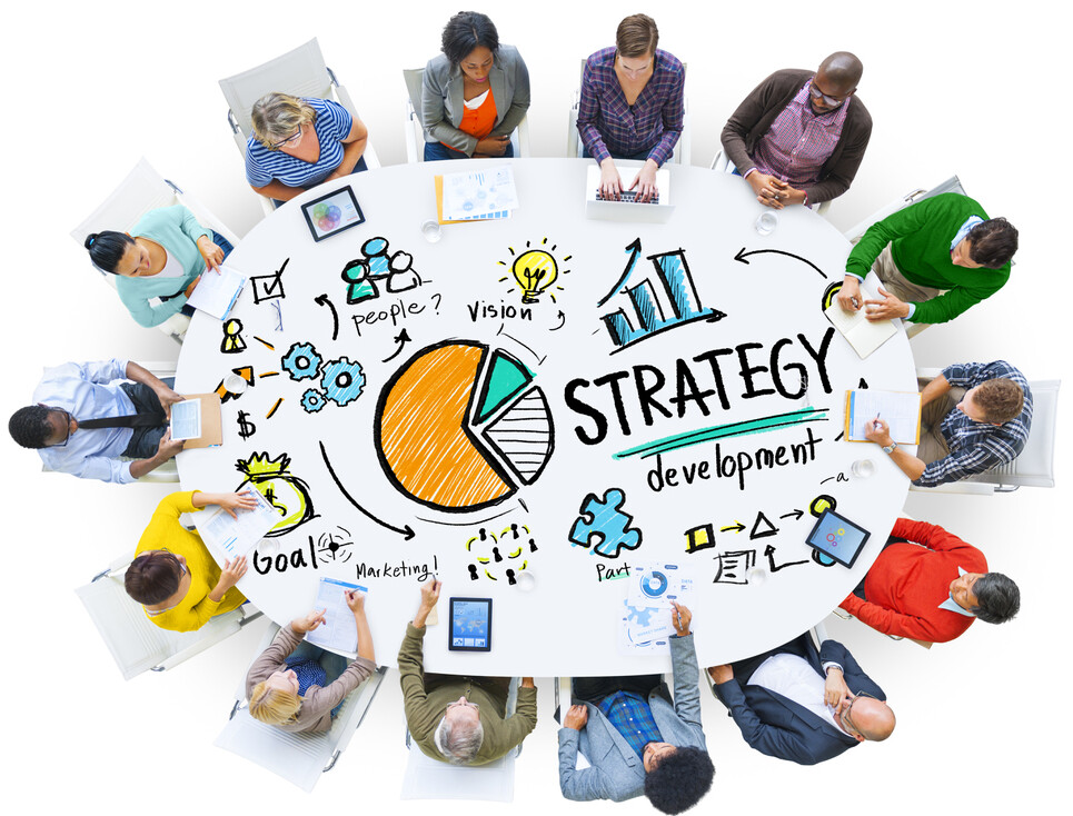 group of adults sitting around oval table with words written on table like strategy, goal, development, and people