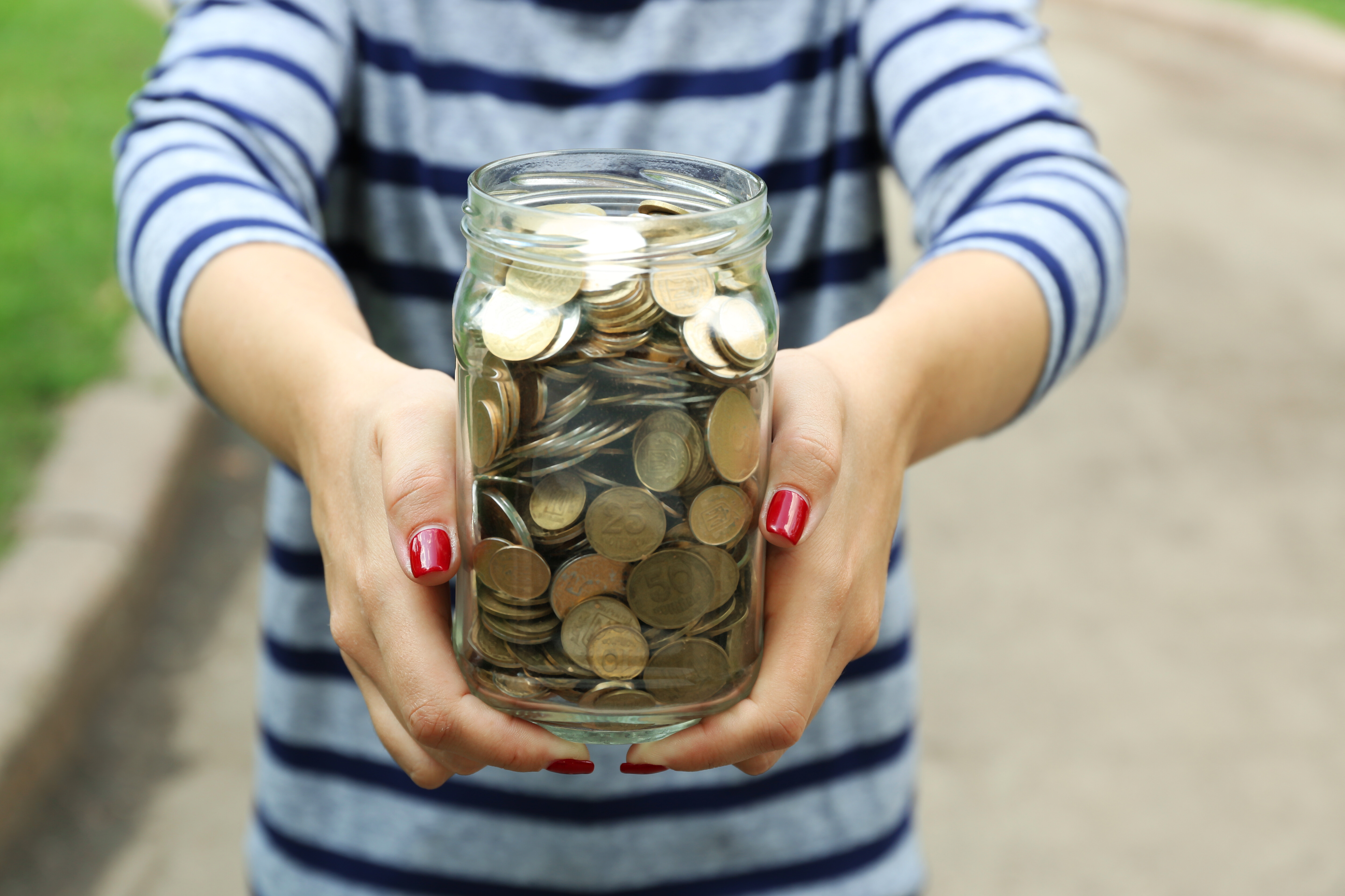 woman's hands holding a mason jar filled with coins. her arms are outstretched towards viewer