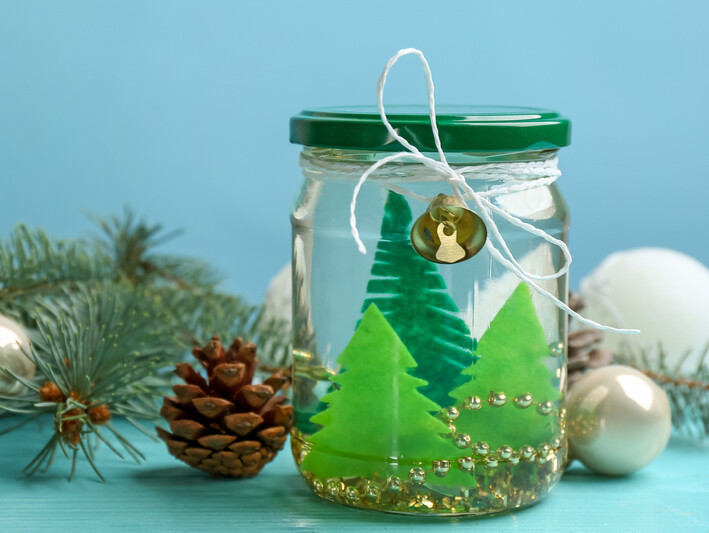Upcycled cleaned pickle jar with cut out felt trees inside it and a string of gold beads tied off with string used as a centerpiece…