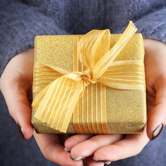 white hands holding golden wrapped box outstreched as if preseting gift