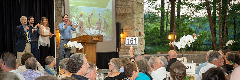 auction at an outdoor stage with people speaking to a crowd