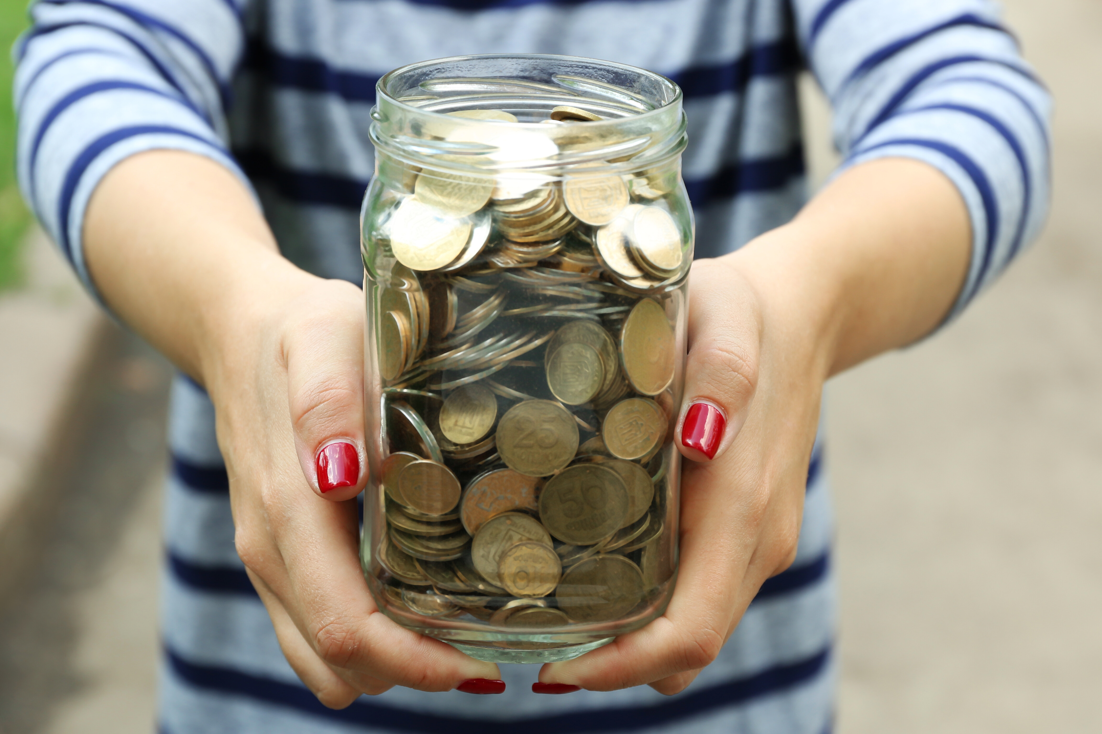 womans hands holding glass jar filled with change 