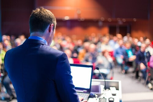 person speaking at a podium in front of crowd at an auction